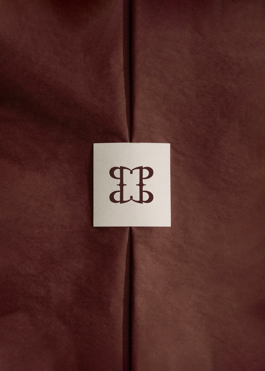Étiquette avec le monogramme de Parfum d'Éthique sur un tissu bordeaux, identité visuelle de la marque