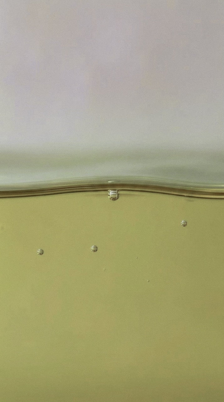 Gros plan sur un liquide ambré translucide avec de fines bulles, évocation de la matière olfactive d'un parfum de niche